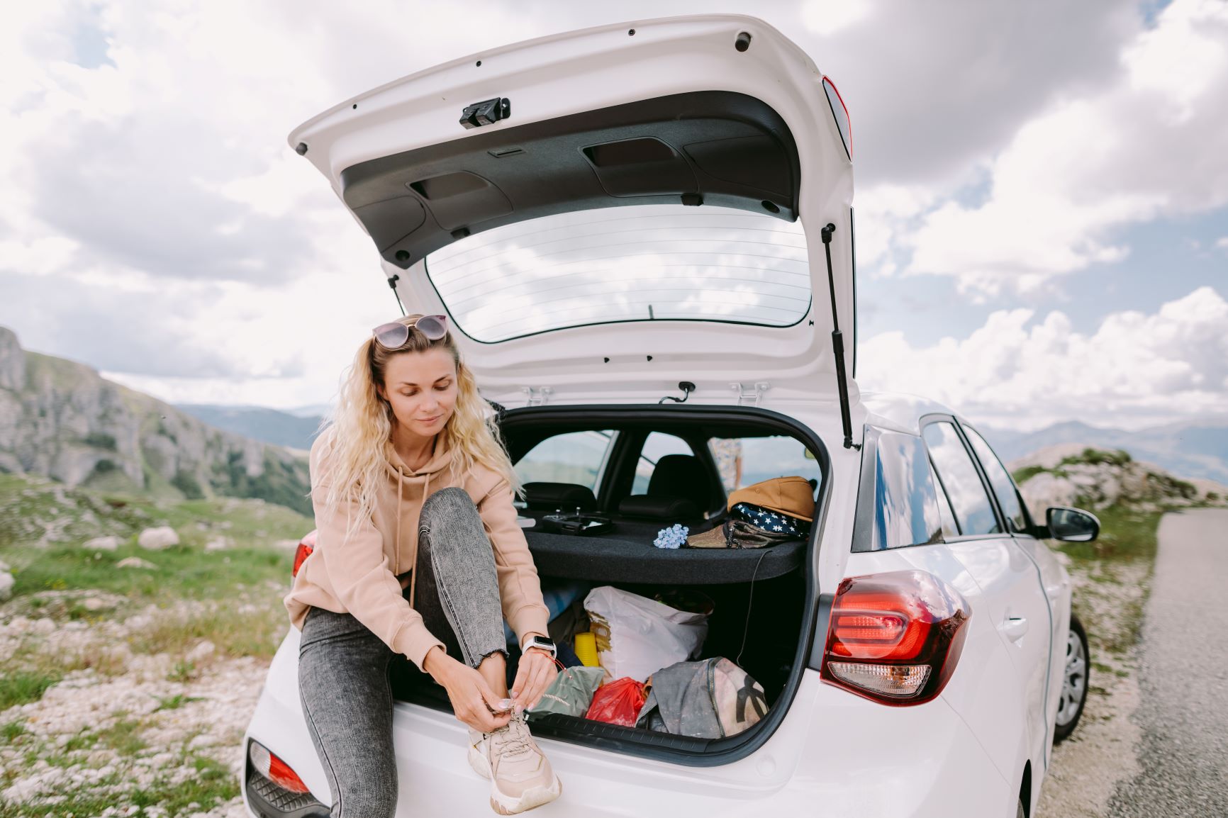 woman tying her shoes leaning on her car