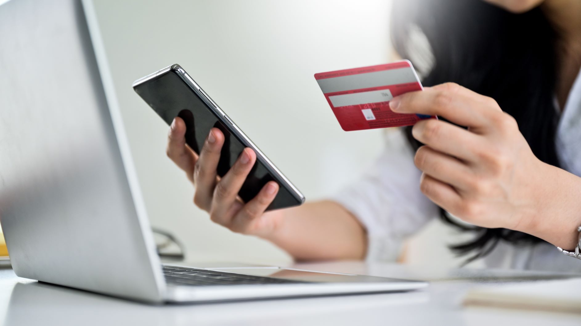 woman holding credit card and phone next to laptop