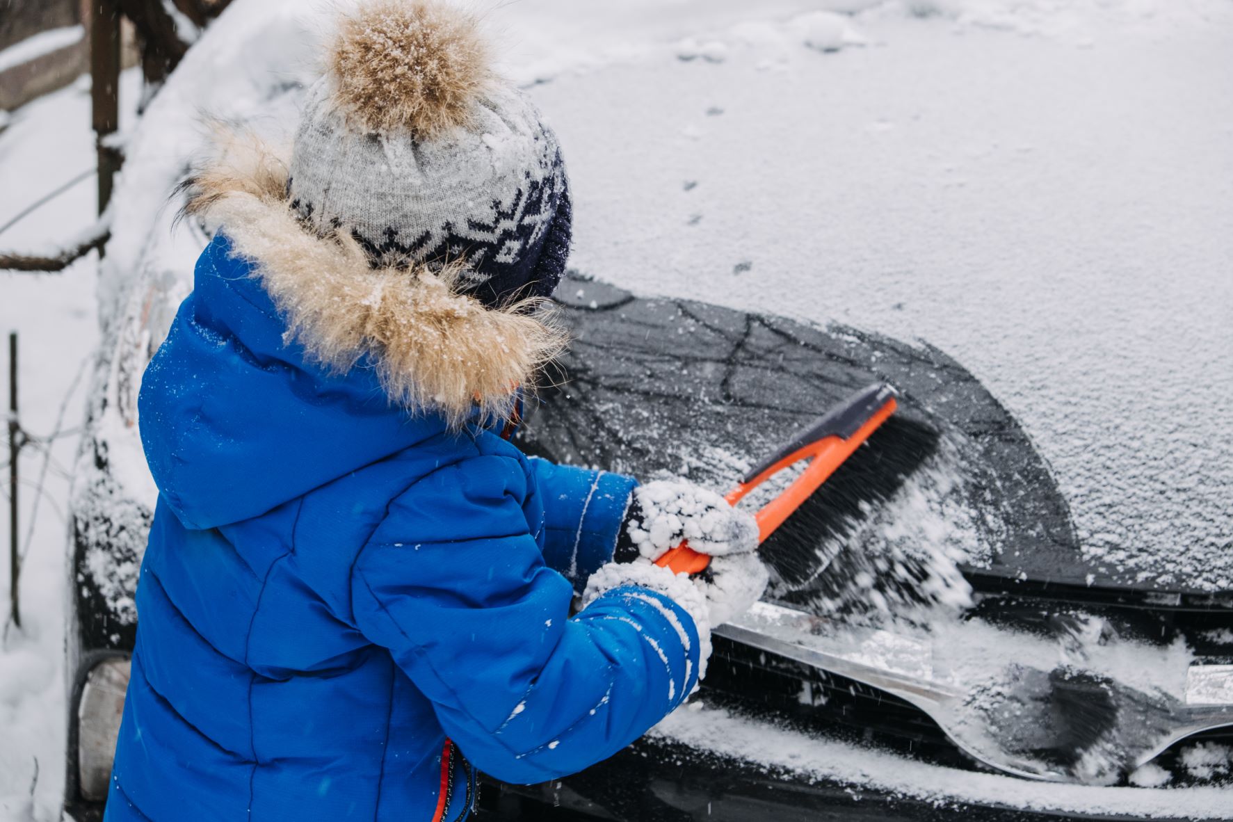 Young kid cleans off snow from car in winter