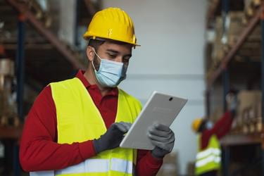 Warehouse employee wearing a facemask and using a tablet