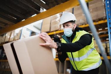Warehouse worker wearing facemask scanning a box