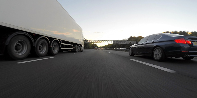 Freight truck and sedan drive along highway.