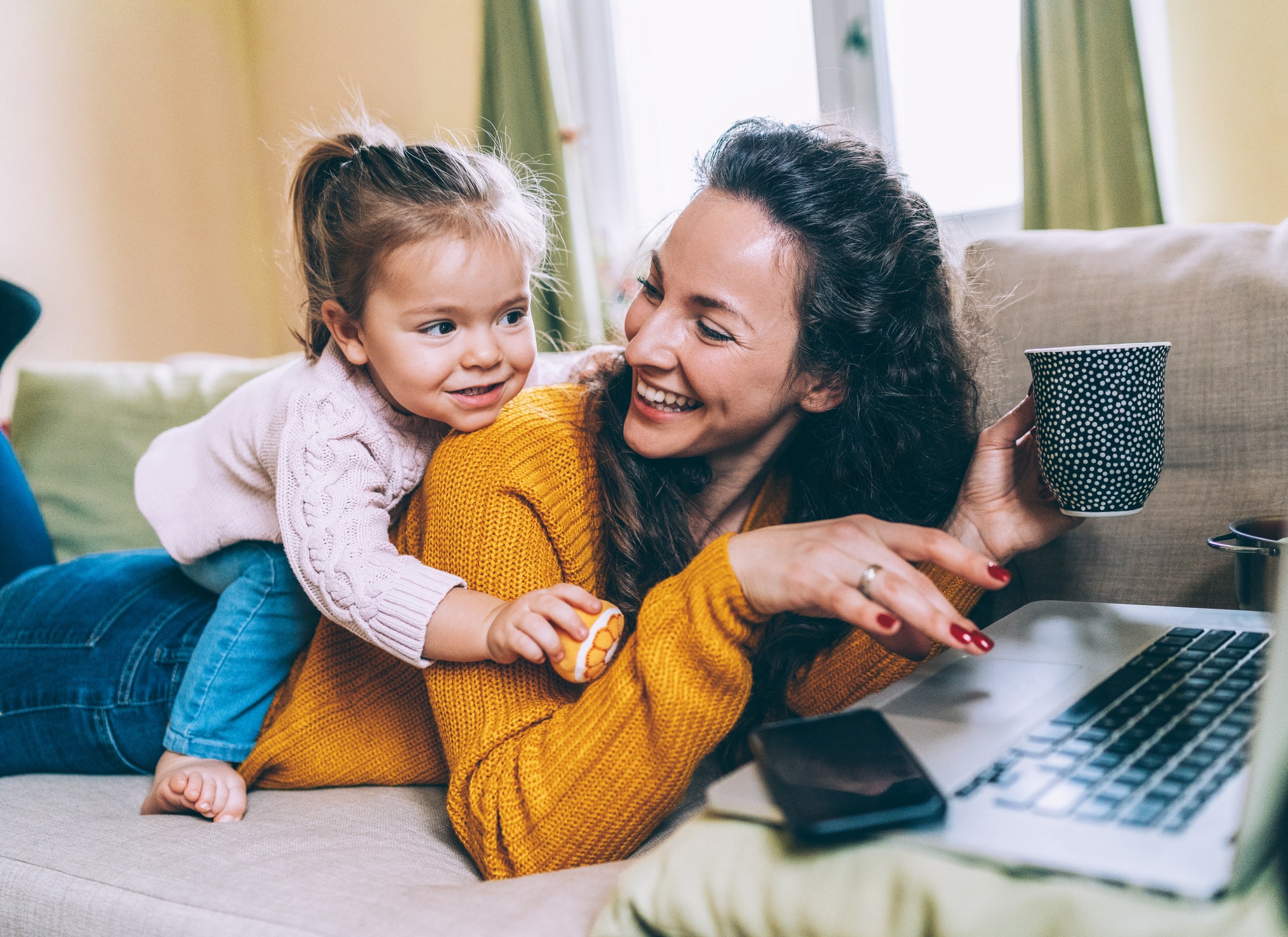 Woman playing with daughter while working on laptop