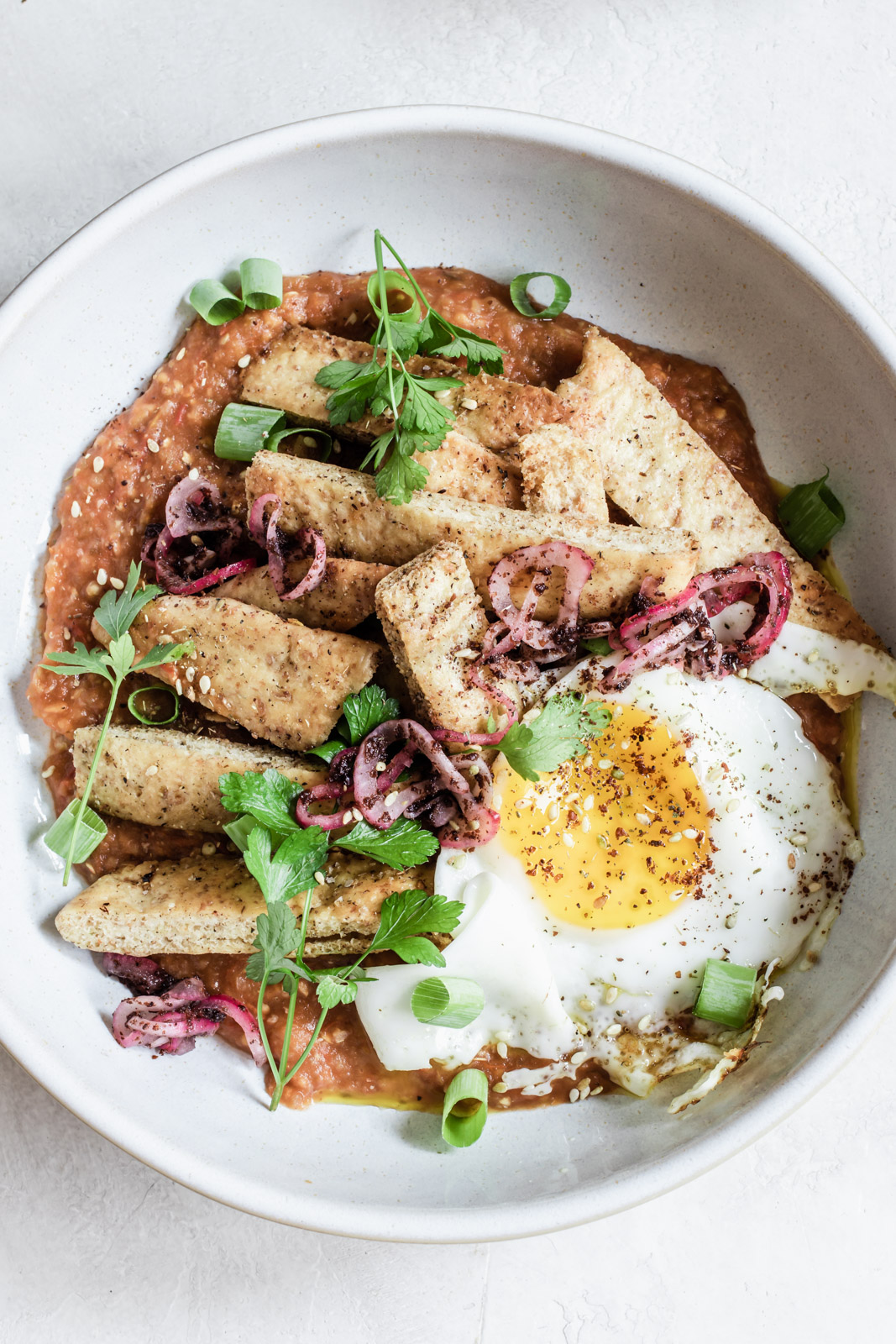 close-up of a bowl of eggplant pitaquiles topped with a fried egg and sumac onions