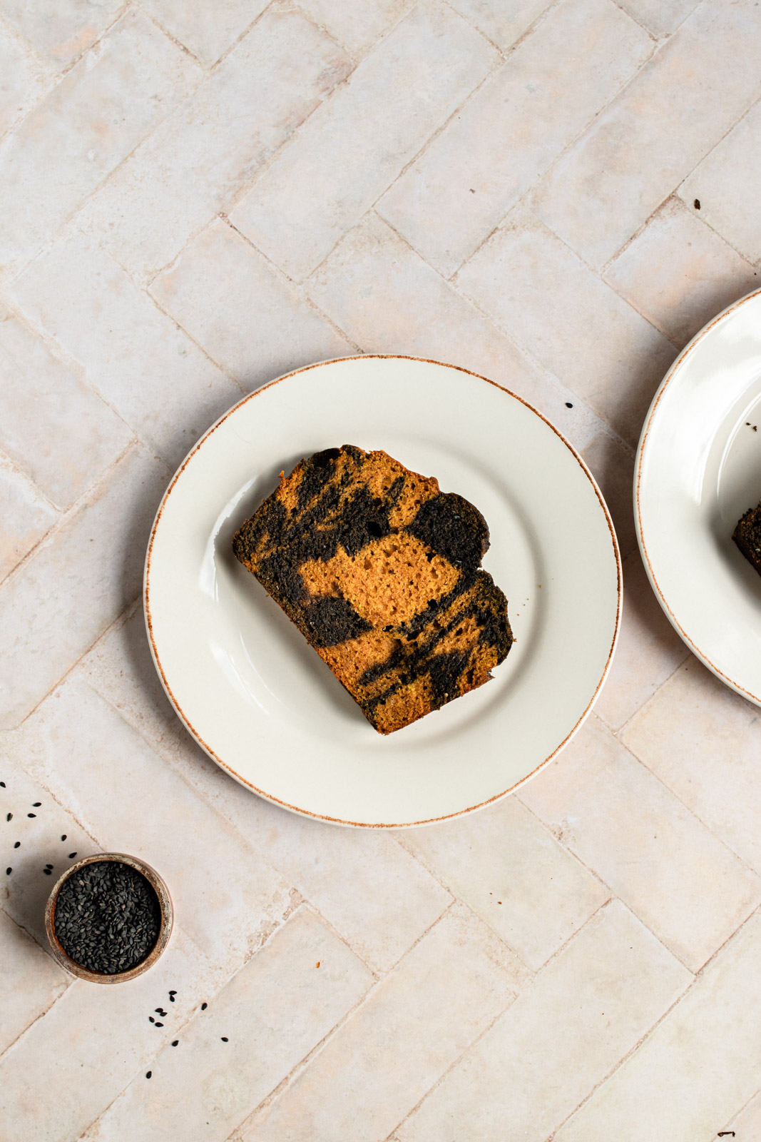 Top-down, two plates each with a slice of black sesame swirl pumpkin bread and a small bowl of black sesame seeds