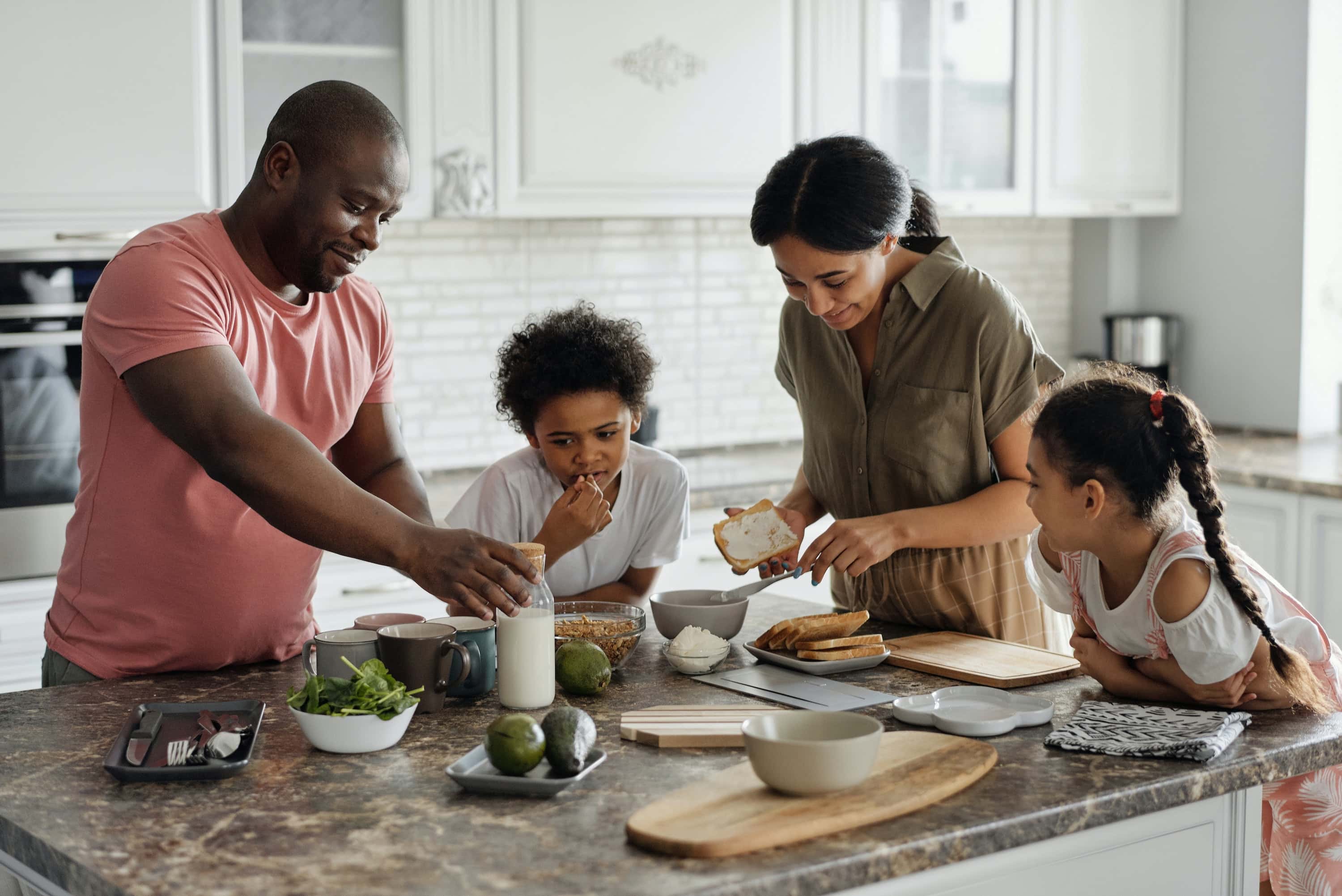 A family gathers at a kitchen island prepping a meal together.