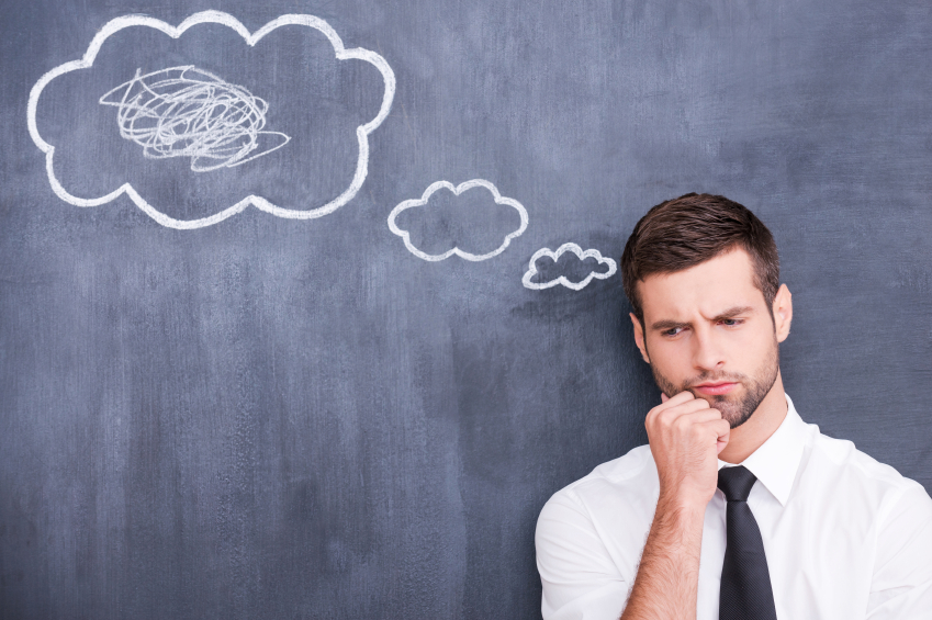 There is a mess in my head. Picture of confused handsome young man holding hand on chin and thinking while standing against cloud chalk drawing on blackboard