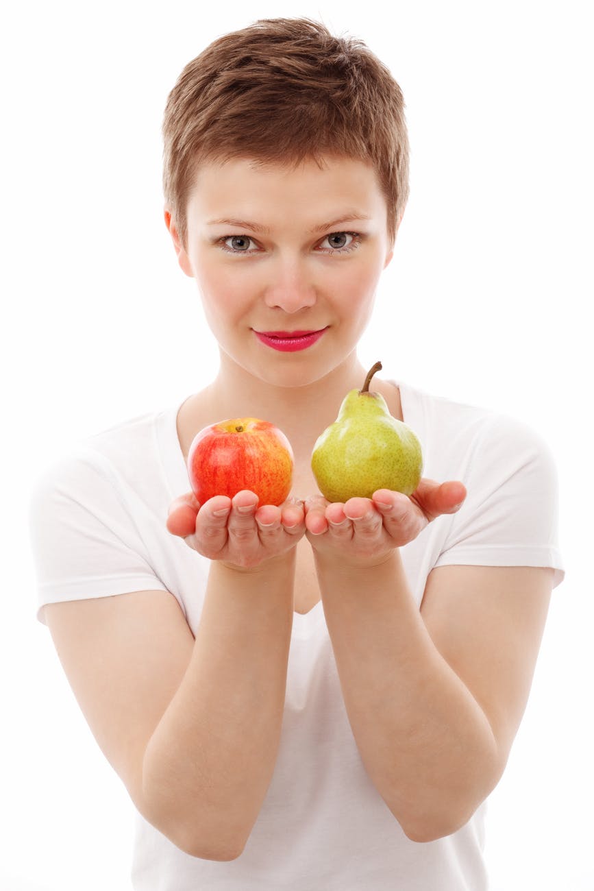 woman holding out two fruits to choose from, an apple or a pear.