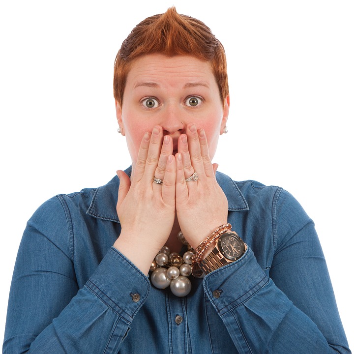 shocked expression on woman with short red hair, hands covering mouth
