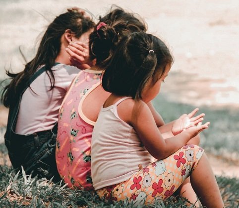 three children sitting very close together in a grassy field