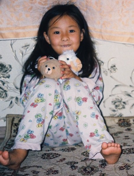 little girl in pajamas sitting in blanket fort under table holding stuffed animals
