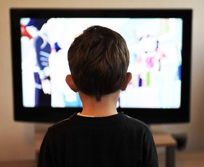 rear view of child watching tv, soft focus television in background