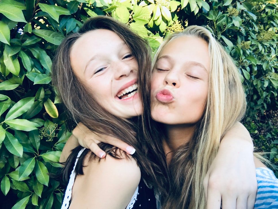two long haired girls hugging and smiling and posing, heads close together for selfie.
