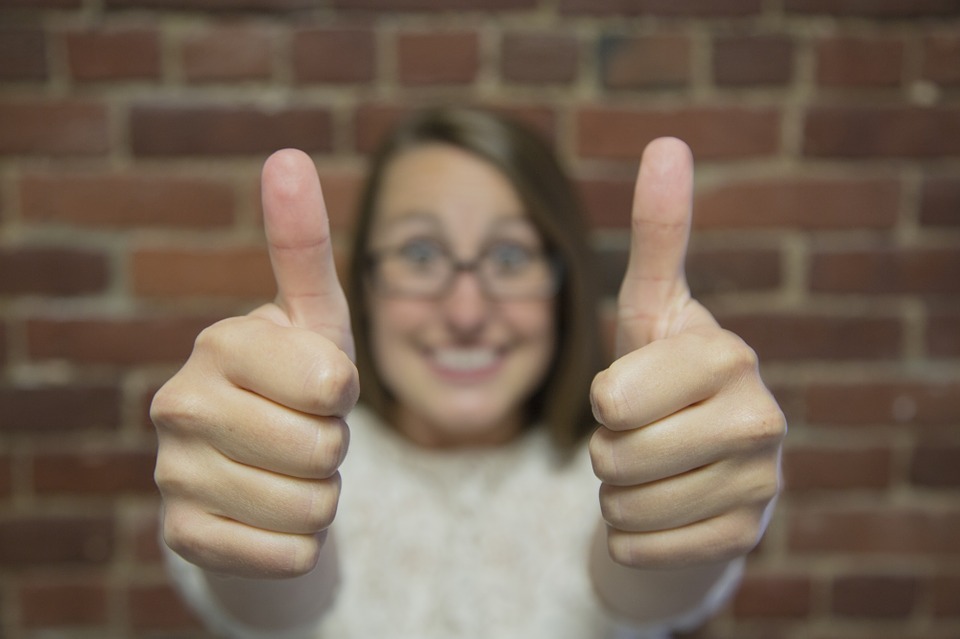 close image of two fists giving thumbs up sign by soft focus smiling woman in background.