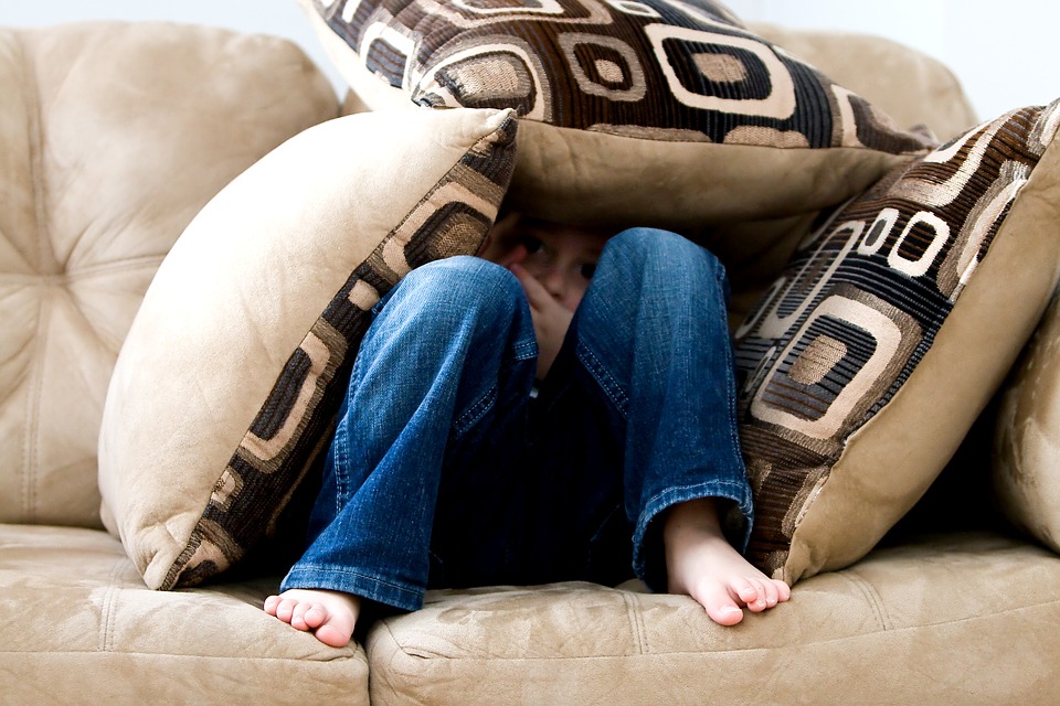 child peeking out of tented throw pillows on couch.