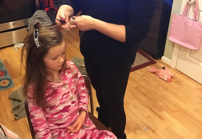 LiceDoctors Technician treating young girl with long brown hair and pink camo pajamas.