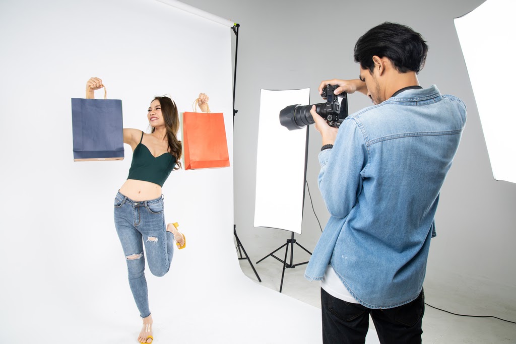 Photographer takes a picture of smiling woman holding shopping bags in professional studio.