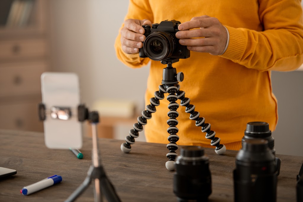 Man adjusts camera on small tripod next to an assortment of camera lenses.