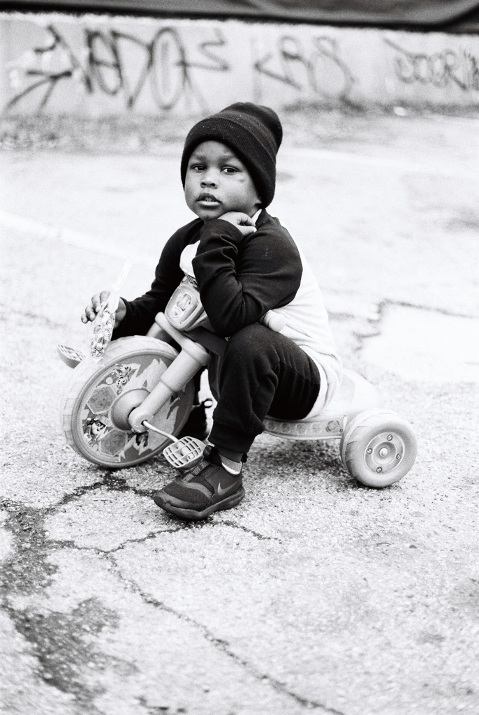 Young black boy sitting out side on his big wheel
