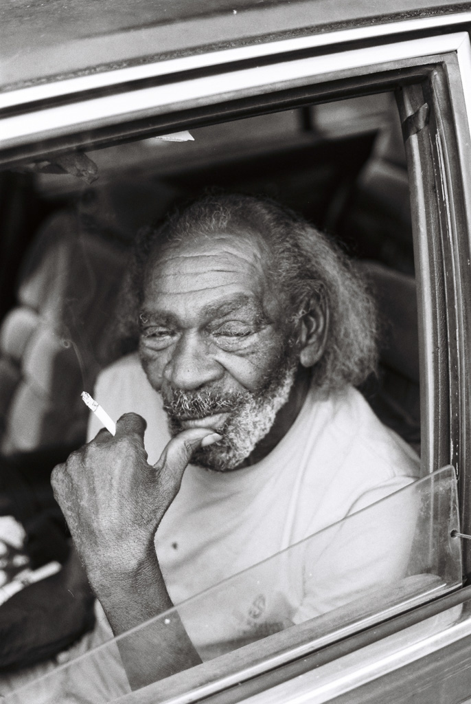 Black man sitting in Oldsmobile holding cigarette