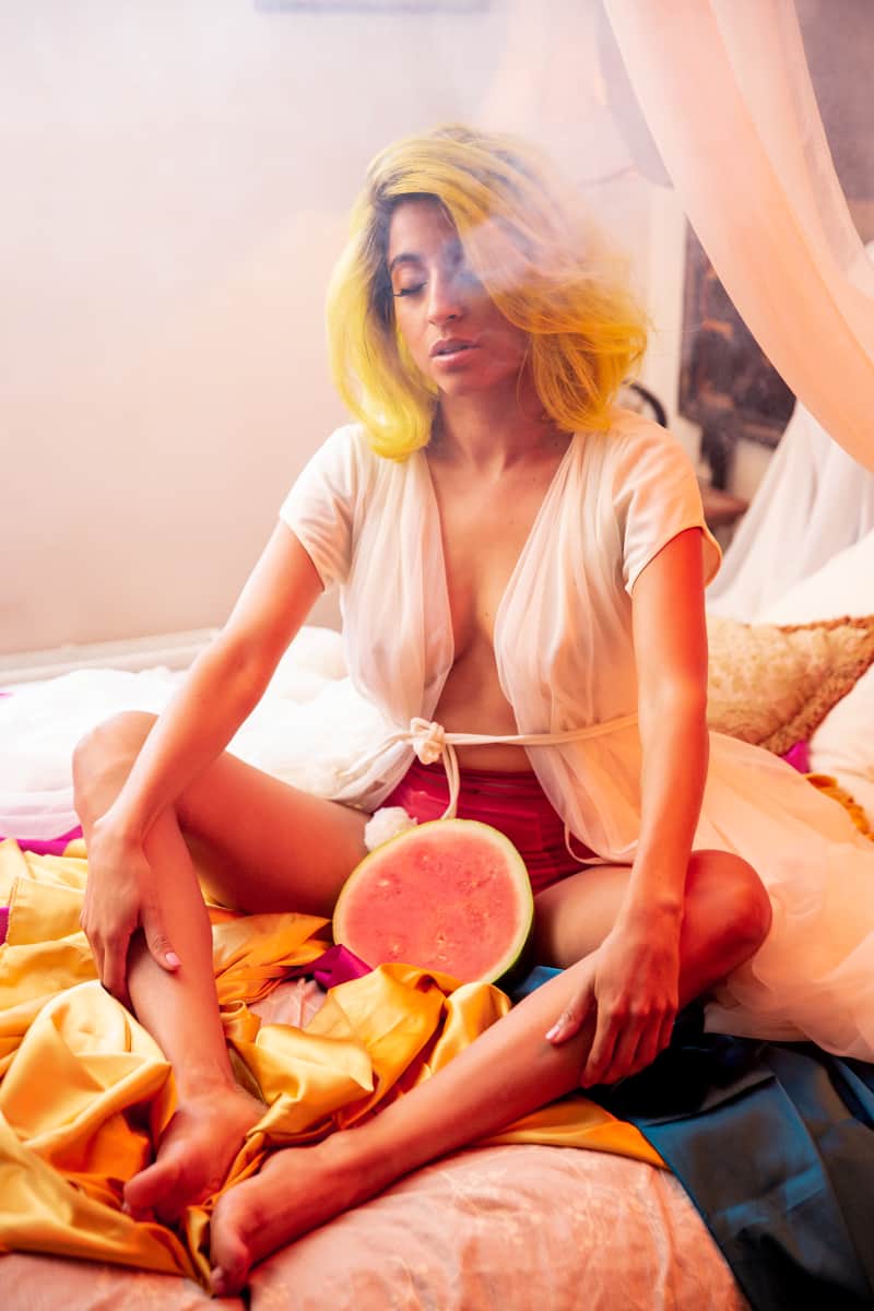 La Lulu sitting on bed with half watermelon between her legs.