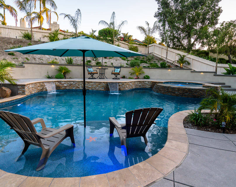 Freeform pool with two lounge chairs and an umbrella in the water.
