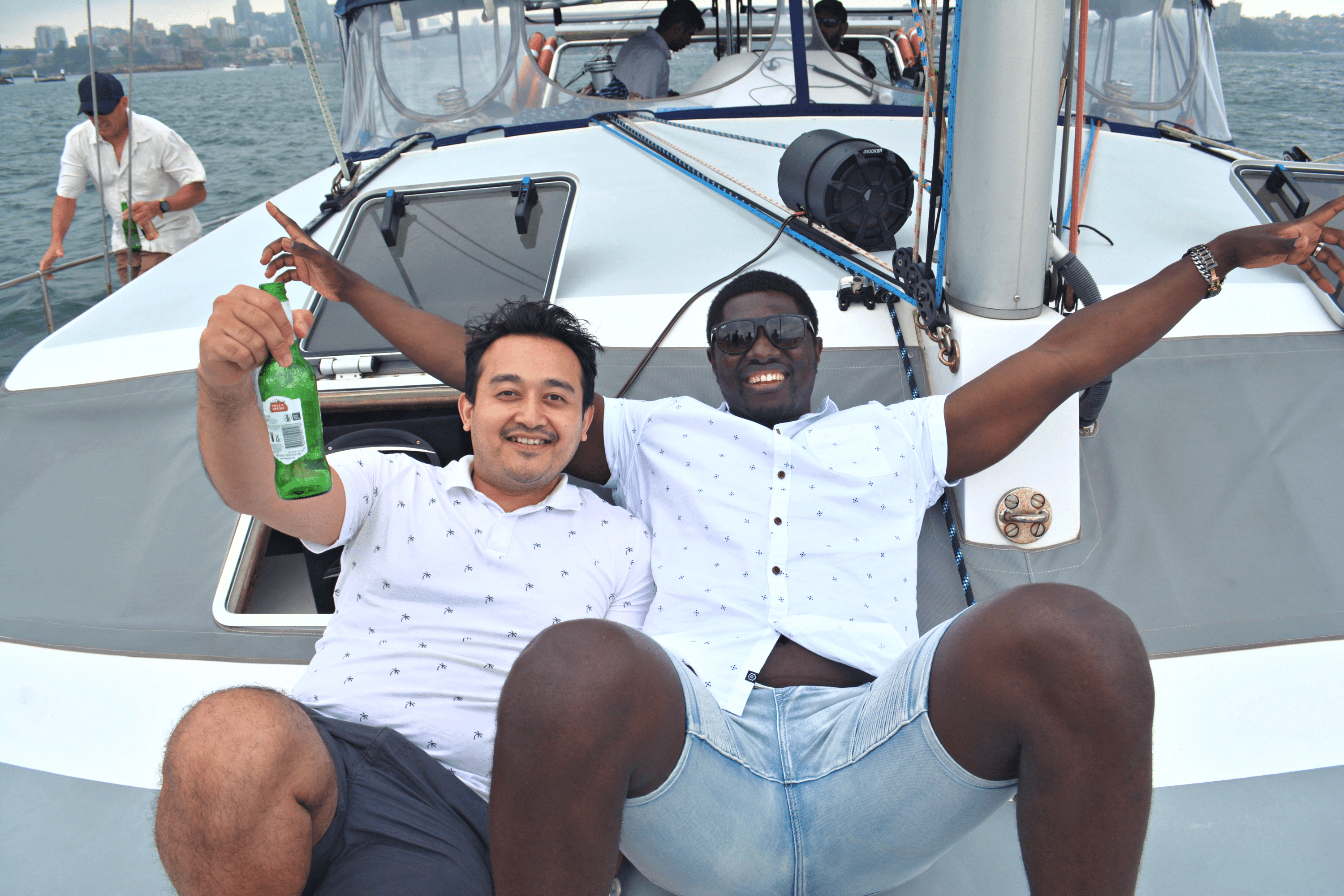 Two men posing with a beer and arms outstretched on a boat