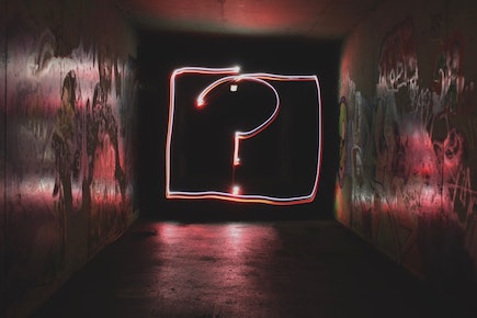 in a graffitti covered walkway, light forms the shape of a question mark