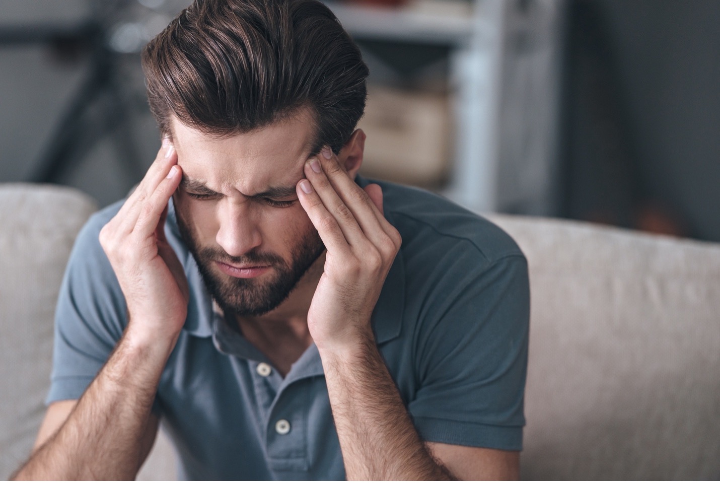 A man with hands on the side of his head has a headache after binge drinking