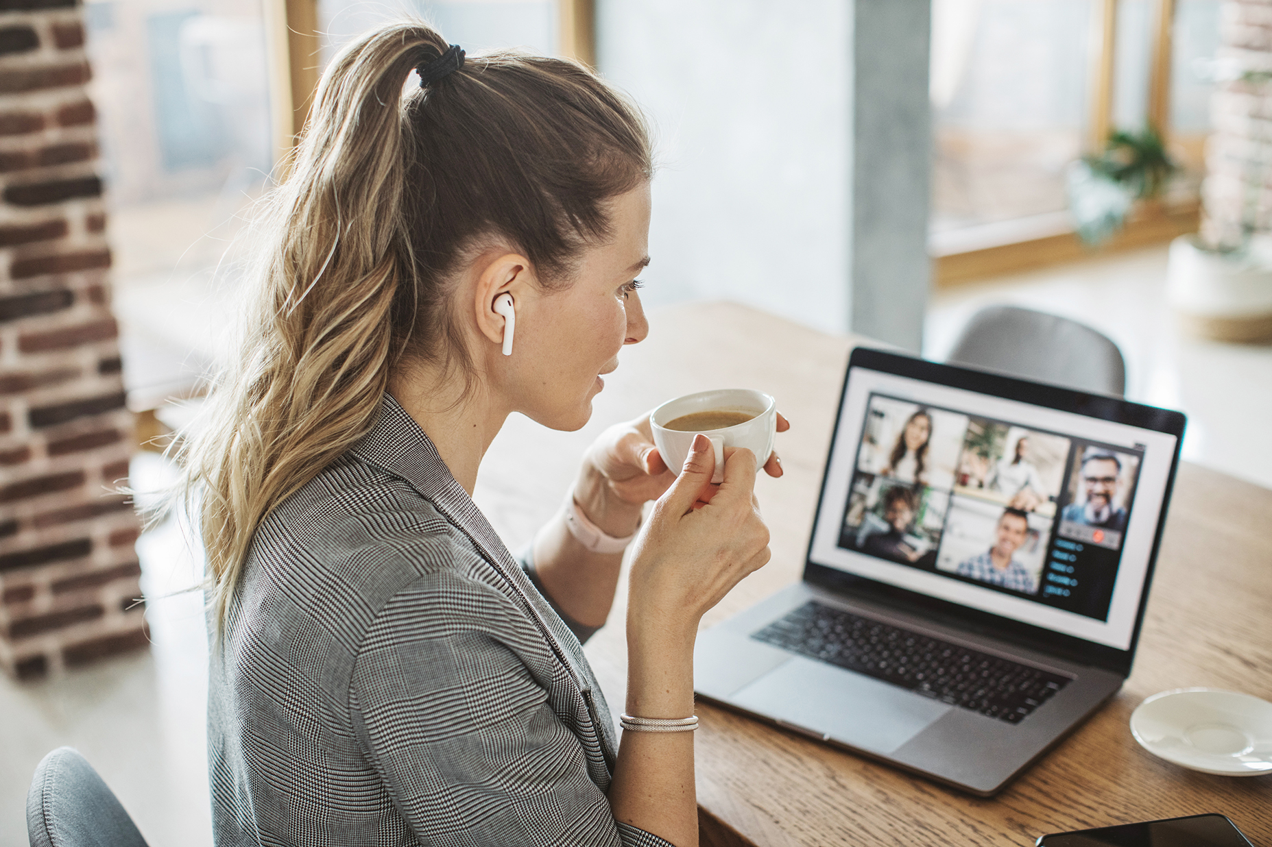 A woman drinks coffee while on a video chat with her alcohol support group
