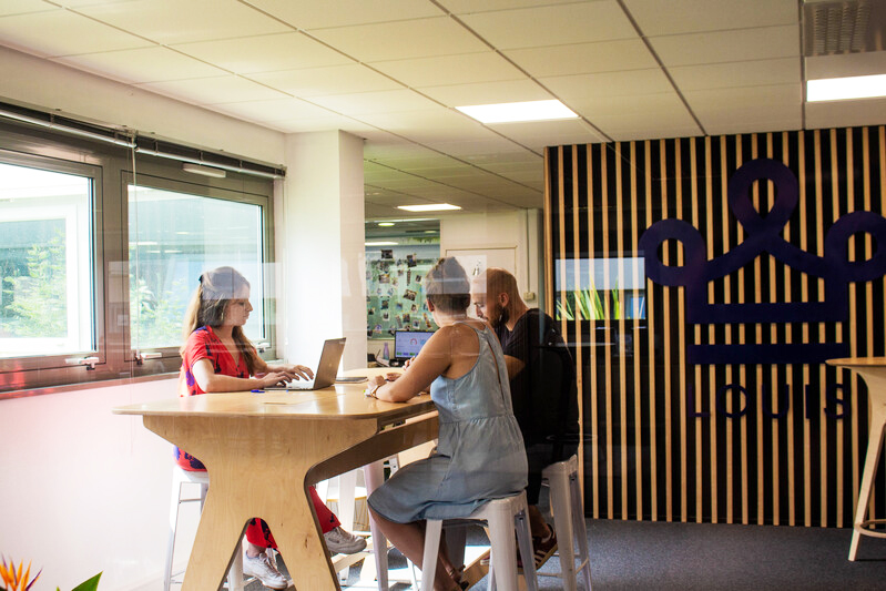 3 personnes assises autour d'une table de réunion haute pour nommer un responsable déménagement dans un bureau décoré avec une couronne LOUIS bleu sur le mur du fond