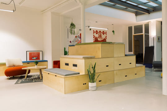 Espace déténte au bureau avec une table basse, un fauteuil et une estrade en bois accompagnée de coussins.
