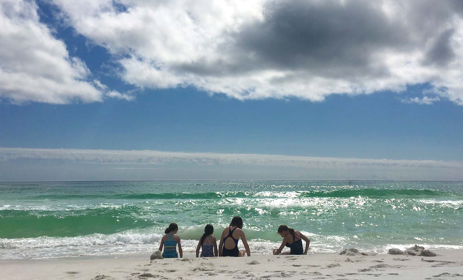 Four girls sitting by emerald ocean at Grayton Beach State Park, Florida