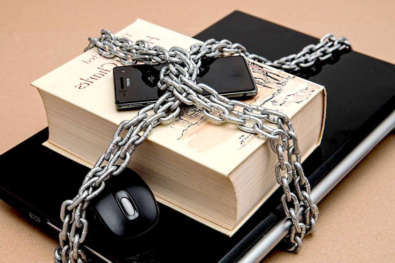 Imagem de um livro, celular e notebook acorrentados ilustrando alguma prática de censura