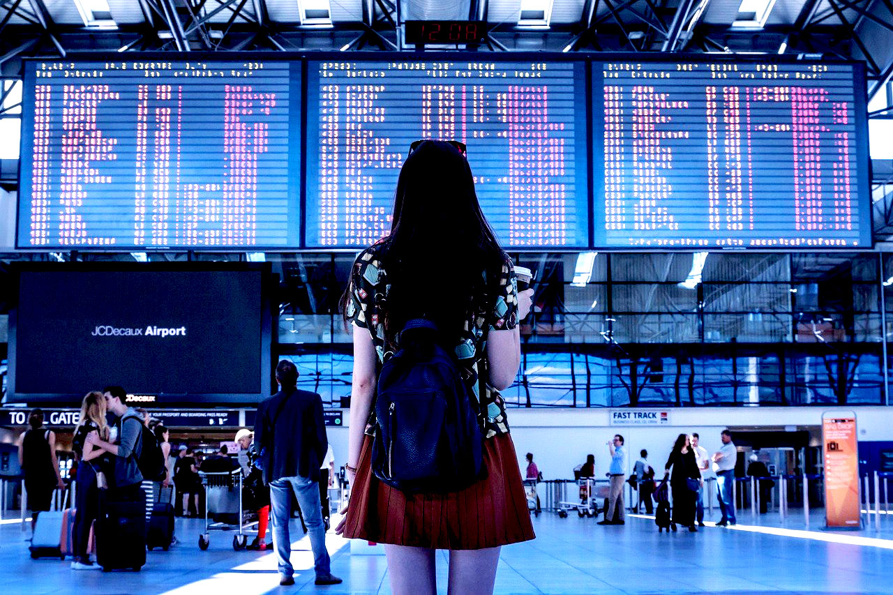 Imagem de uma mulher observando o painel de voos em um aeroporto