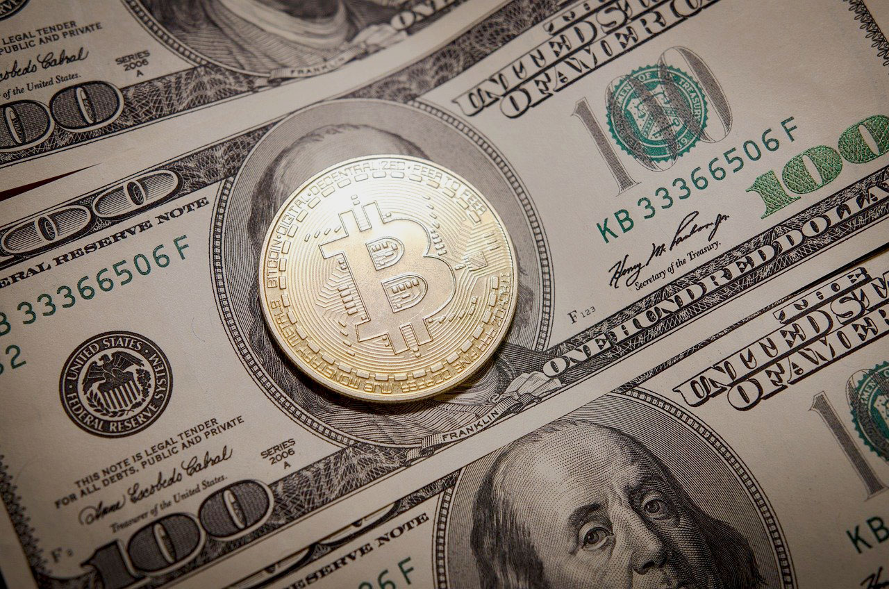 Imagem de uma moeda de bitcoin sobre uma nota de dólar