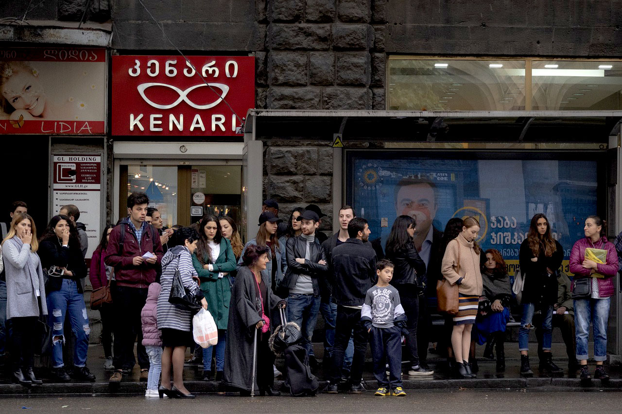Imagem de pessoas esperando o transporte publico em frente de comércios em Tbilisi