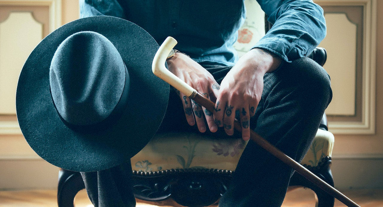 Imagem de um homem sentado com um chapéu e uma bengala
