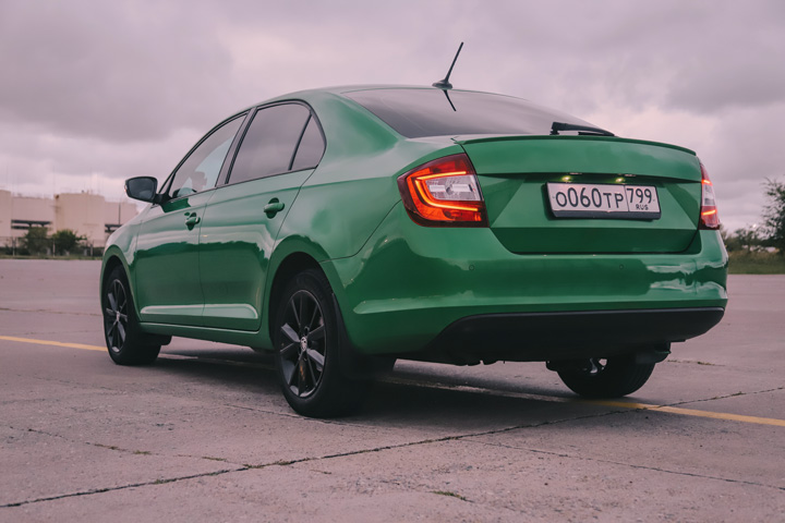 Carro sedã verde estacionado em pátio sob céu nublado
