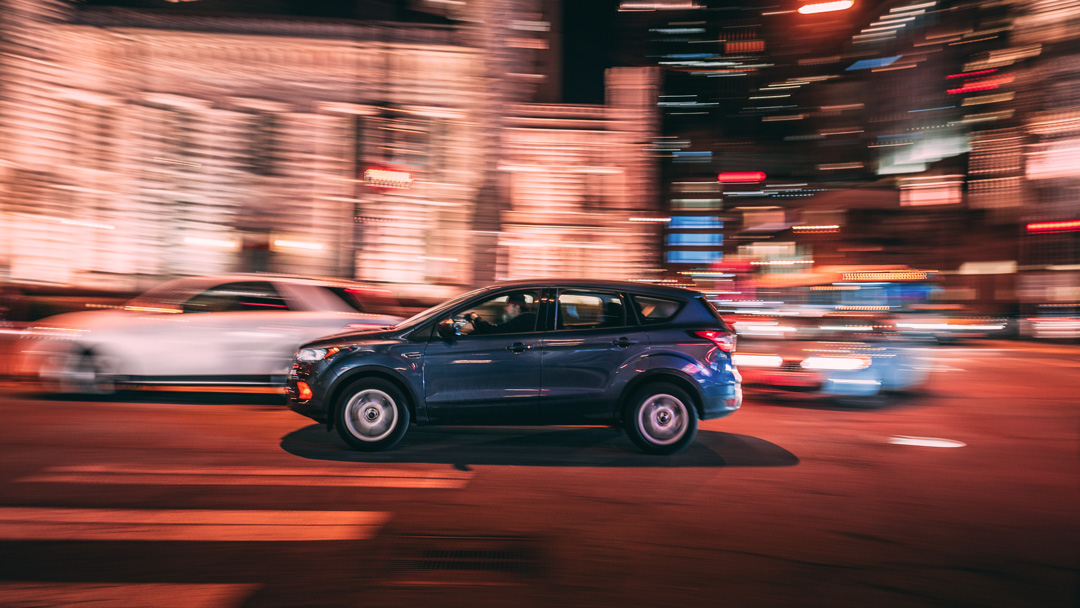 Carro SUV andando pela rua iluminada da cidade durante a noite