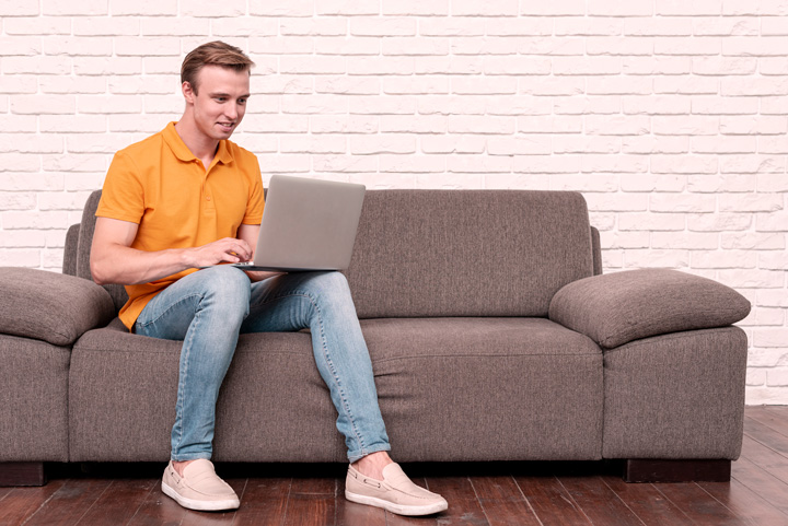 Homem jovem em sofá de sua casa usando notebook para comprar carro na Carupi
