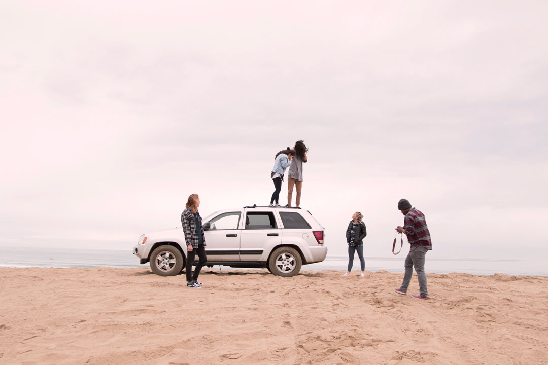 Jovens na praia se divertindo e subindo em cima de um carro SUV