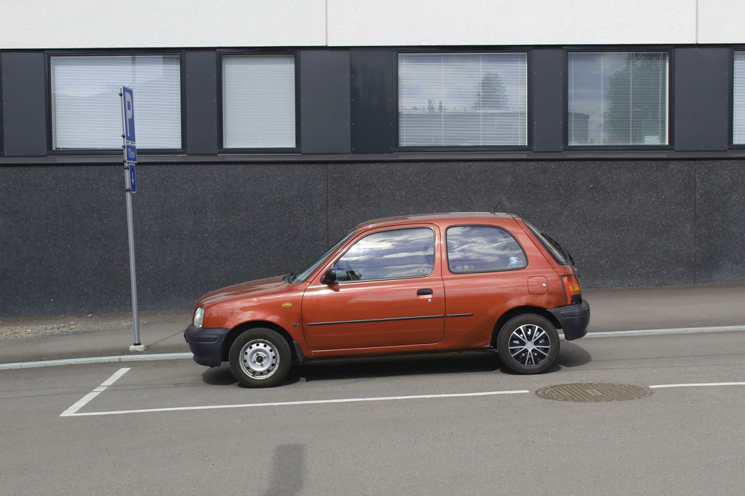 Carro hatch compacto estacionado em ladeira em frente a placa de trânsito
