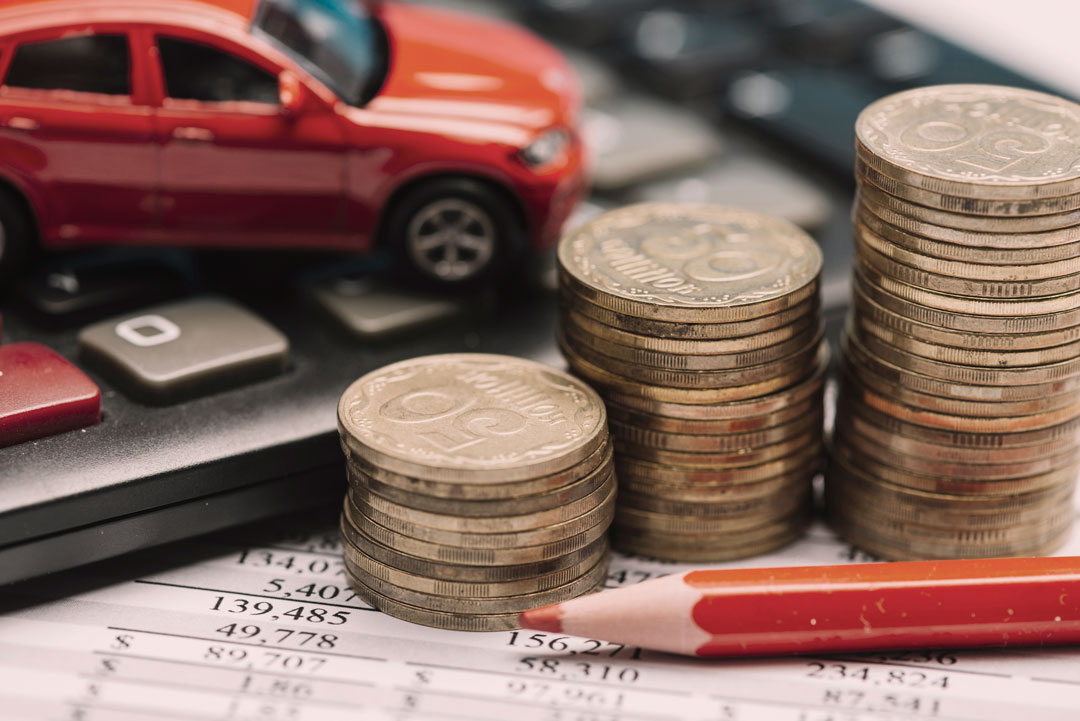 Planilha de cálculos, calculadora, lápis e moedas empilhadas junto a miniatura de carro