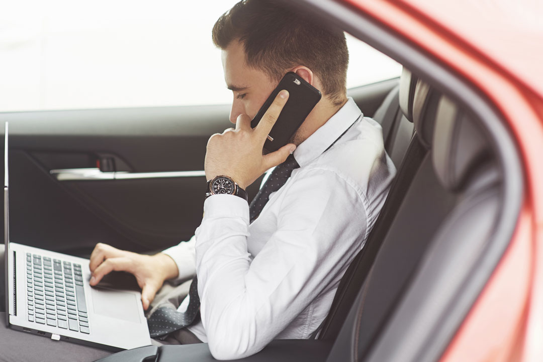 Executivo em banco traseiro de carro trabalhando em laptop e falando ao celular