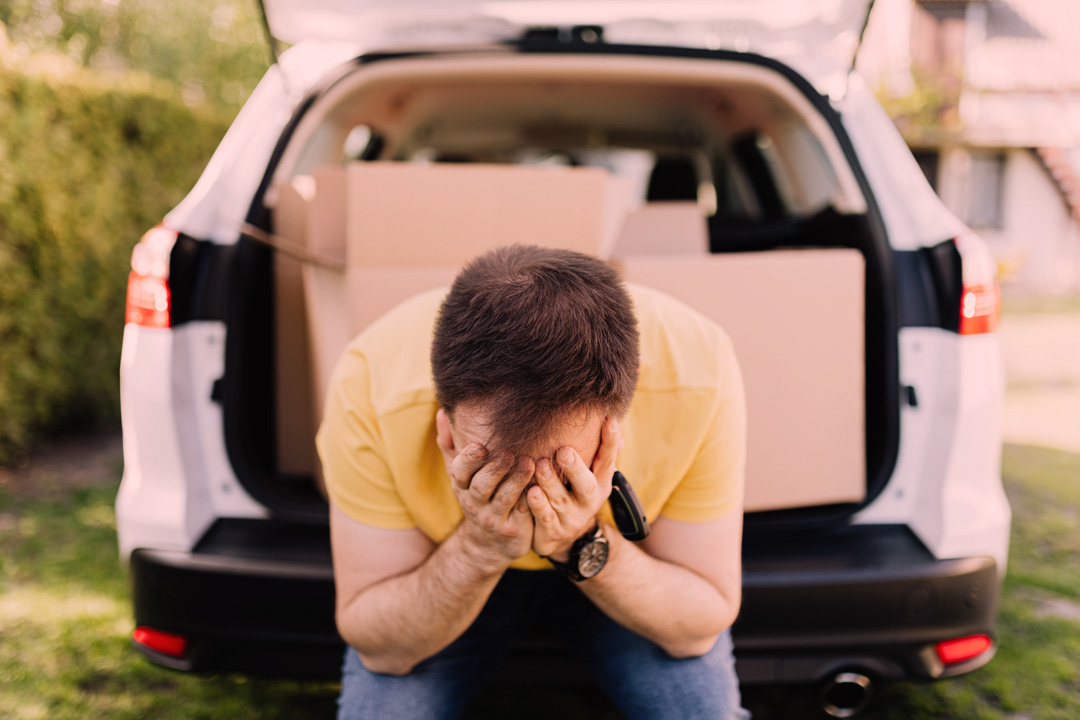 Homem triste sentado no porta-malas de seu carro