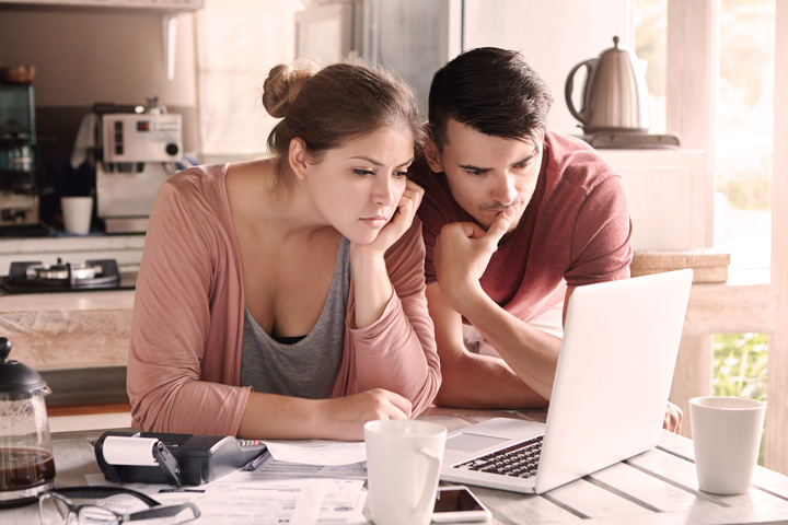 Casal fazendo cálculos e pagando contas de forma digital em computador laptop