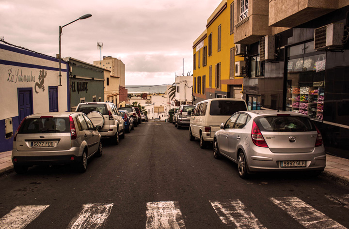 Rua central de cidade com diversos carros estacionados nos dois lados