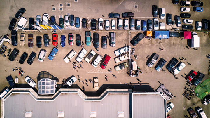Visão aérea de estacionamento de shopping com muitos carros ocupando vagas ao ar livre