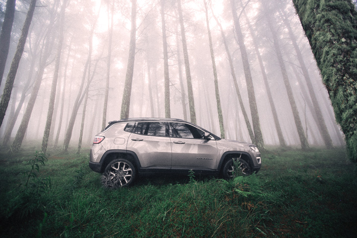 Jeep Compass em meio a floresta com raios de sol penetrando pelas copas das árvores